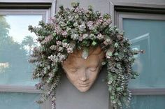 a head with plants growing out of it on the side of a building next to a window