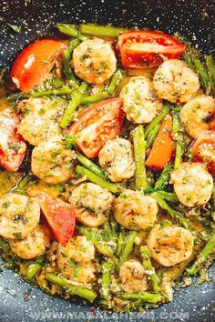 a skillet filled with shrimp, asparagus and tomatoes