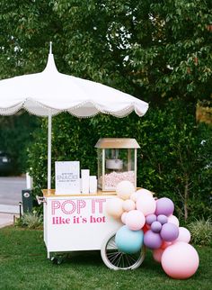 a small ice cream cart with balloons on the side and a white umbrella over it