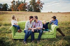 three adults and two children sitting on a green couch in a grassy field with trees