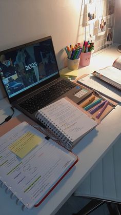 an open laptop computer sitting on top of a desk next to a notebook and pencils