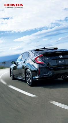 the rear end of a black honda civic hatchback driving on a road with mountains in the background