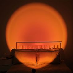 a bed with pillows and an orange light shining on the headboard in front of it