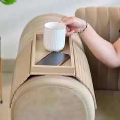 a woman is holding a coffee cup and cell phone on a tray that sits on the back of a couch