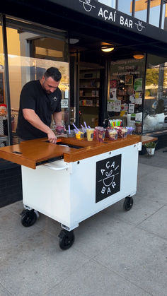 a man standing behind a table with food on it in front of a storefront