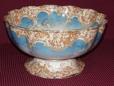 a blue and gold bowl sitting on top of a red tableclothed floor next to a wall