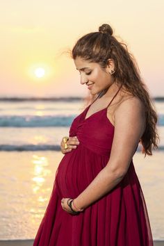 a pregnant woman standing on the beach at sunset