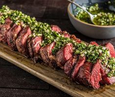 a piece of steak on a wooden cutting board next to a bowl of broccoli