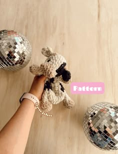 a person holding a stuffed animal in front of two disco ball ornaments on a wooden table