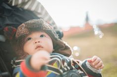 a baby in a stroller pointing at the camera with his hand on the handle