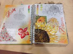 an open notebook with drawings and flowers on the pages, sitting on a wooden table