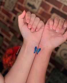 two girls with matching blue butterfly tattoos on their wrists, both holding hands together