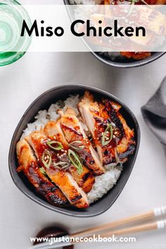 two bowls filled with chicken and rice next to chopsticks on a table top