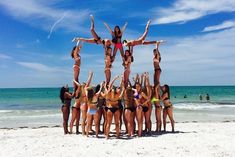 a group of women standing on top of each other in front of the ocean with their arms up