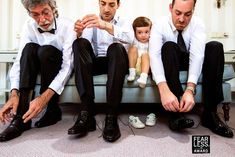 three men are sitting on a couch with their feet in the air and one man is tying his shoelaces