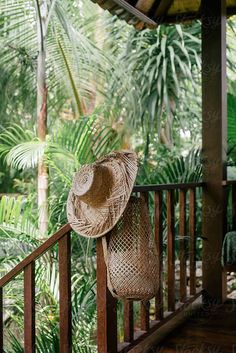 a straw hat sitting on top of a wooden railing in front of trees and plants