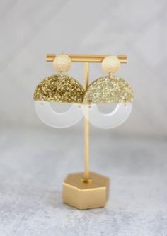 the gold and white earrings are hanging from a metal stand on a marble surface,