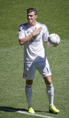 a man standing on top of a soccer field holding a ball in one hand and wearing yellow shoes