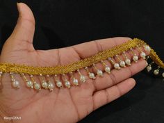 a hand holding a gold chain with pearls on it