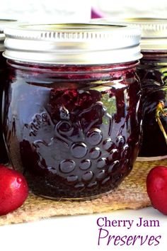 three jars filled with jam sitting on top of a wooden cutting board next to two cherries