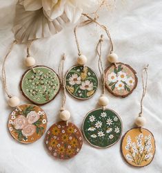 six hand painted wooden ornaments hanging from strings on a white sheet with flowers in the background