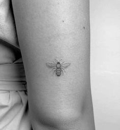 a black and white photo of a small bee tattoo on the right side of the thigh