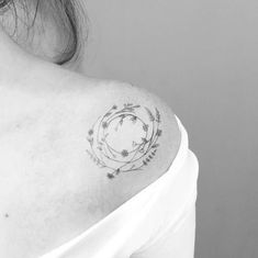 a woman's shoulder with a circle tattoo on it and flowers in the middle