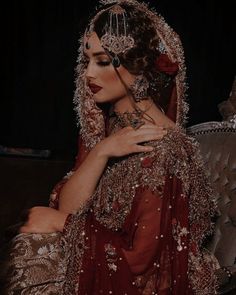 a woman in a red and gold wedding dress is sitting on a couch with her arms wrapped around her head