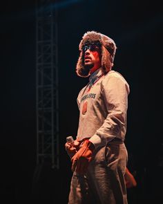 a man wearing a fur hat and coat on stage with his hands in his pockets