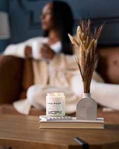 a woman sitting on a couch next to a table with a candle and some reeds