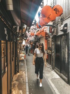 a woman walking down an alley way with orange balloons hanging from the side of buildings