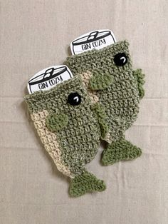 two green crocheted fish mitts with black eyes and one has an eye patch on it