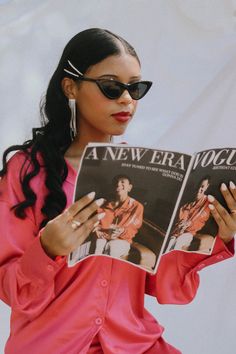 a woman wearing sunglasses reading a new era vocal album in front of a white backdrop