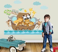 a young boy standing in front of a wall mural with animals on the boat and an old blue toy car