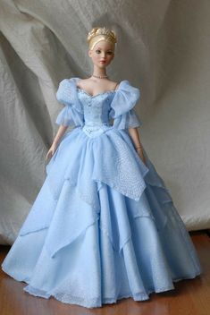 a doll dressed in a blue gown on a wooden floor next to a white backdrop