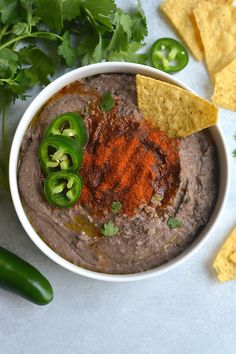 a white bowl filled with black bean dip surrounded by green peppers and tortilla chips