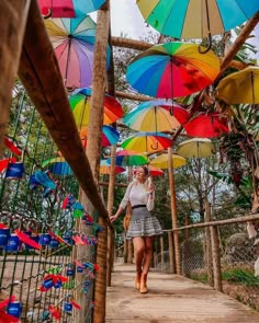 a woman walking down a wooden walkway covered in colorful umbrellas