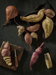 several different types of vegetables on a black surface with a brush and knife next to them