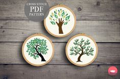 three cross stitch trees with leaves on them are hanging from wooden hoops against a wood background