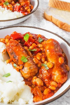 two plates filled with meat and beans next to rice on a white table cloth,