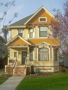 a yellow house with brown trim on the front porch and stairs to the second floor