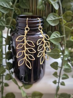 a pair of gold leaf earrings sitting on top of a vase filled with green leaves