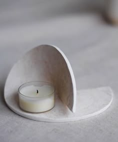 a white candle sitting on top of a table next to a small glass container with a lit candle in it