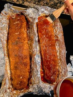 two fish fillets sitting on top of tin foil next to a cup of sauce