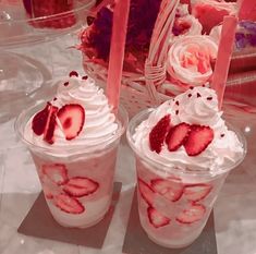 two dessert cups with strawberries and whipped cream in them sitting on a table next to flowers