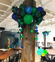 balloons are hanging from the ceiling in an open space with wooden tables and black chairs