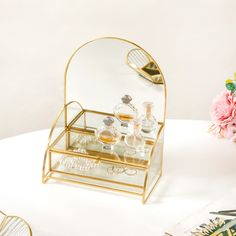 a vanity mirror with some glasses on it next to pink flowers and other items in front of it