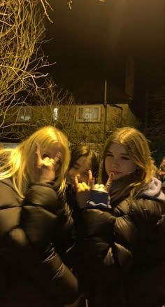 two women standing next to each other in front of a building at night with their fingers up