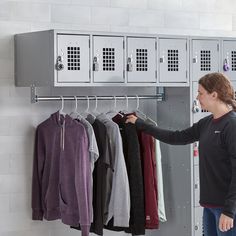 a woman standing in front of a metal locker with lots of clothes hanging on it