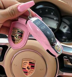 a woman holding a pink car keychain in front of a steering wheel and dashboard